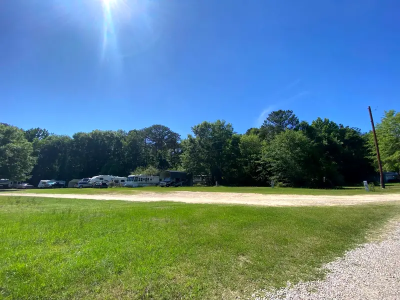 A long grass field with a row of campers along the tree line